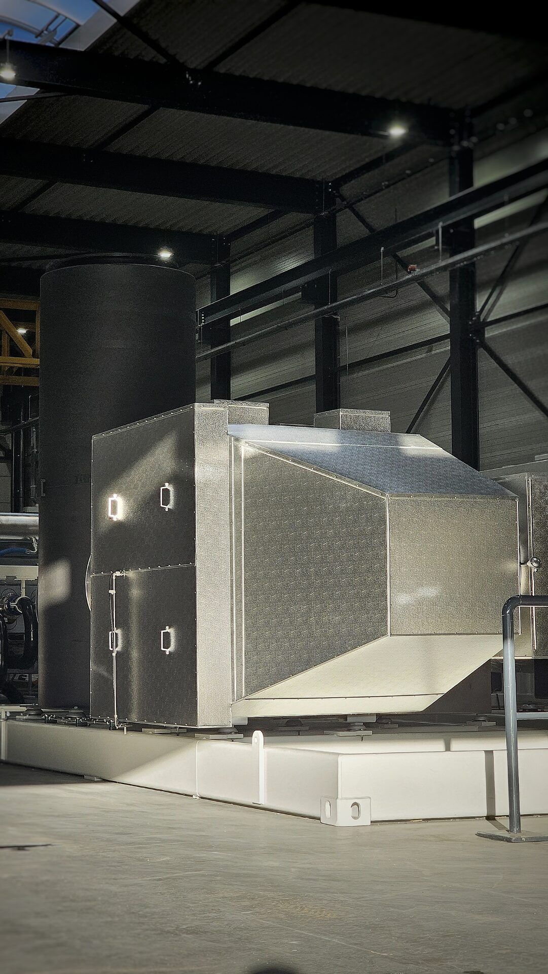 Geluidsgeïsoleerde uitlaatdemper van geribd aluminium plaatwerk naast een zwarte geluidsdemper in een productiehal