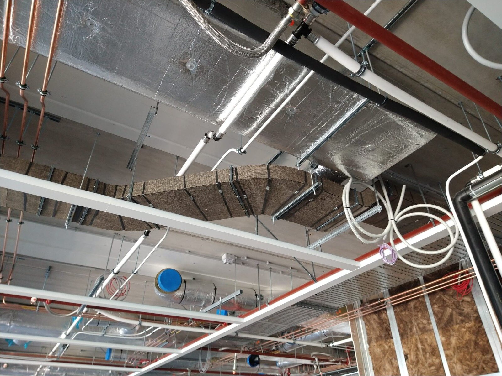 Luchtkanalen met aluminium- en steenwolisolatie tussen leidingen onder een plafond in aanbouw