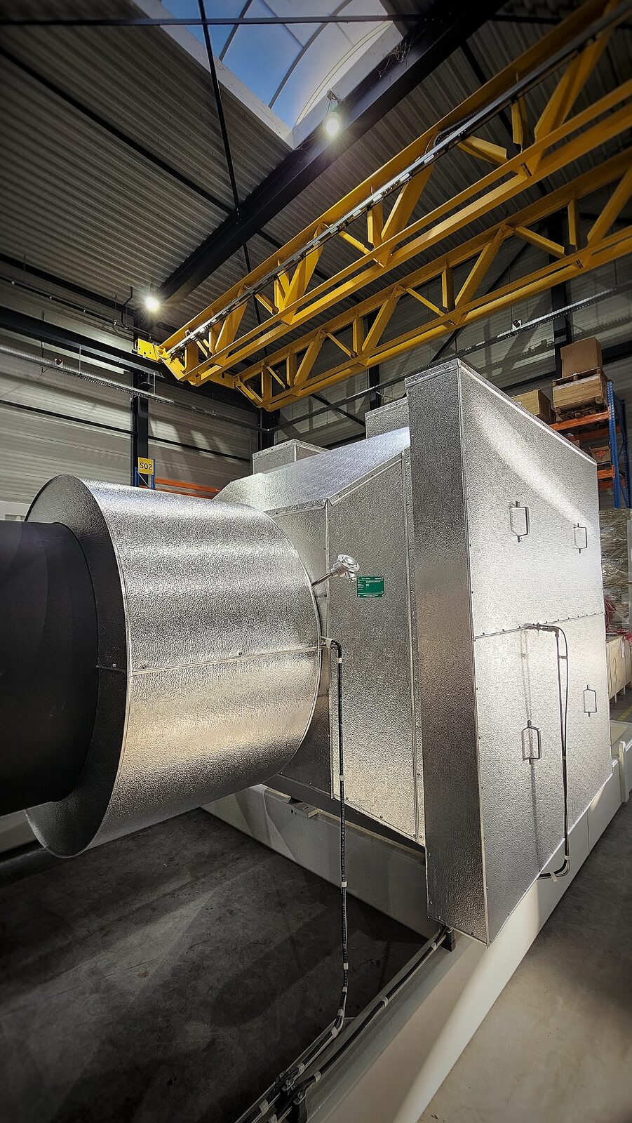 Ronde en rechthoekige ommanteling van aluminium plaatwerk op een uitlaatsysteem onder een gele rolbrug