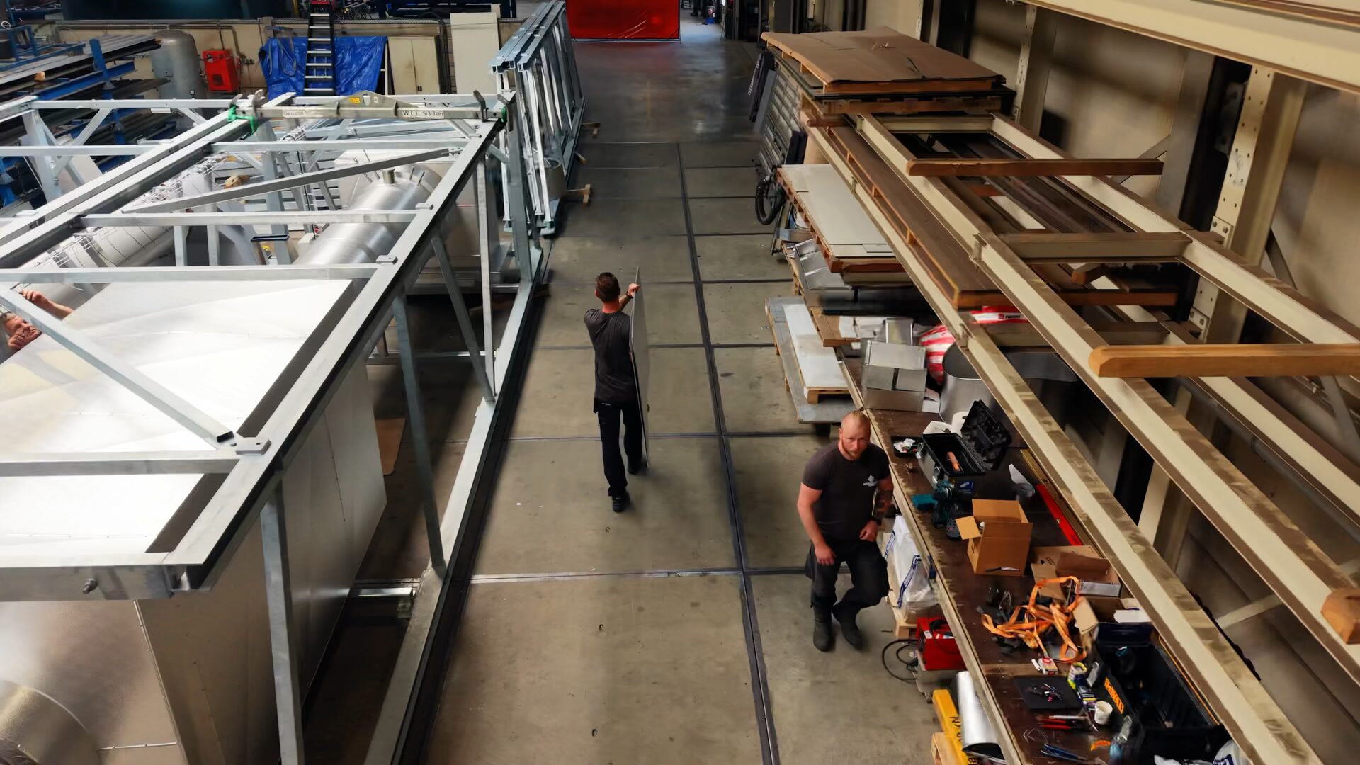Twee medewerkers in de werkplaats tussen stellingen met plaatmateriaal en een stalen frame met geïsoleerde tanks