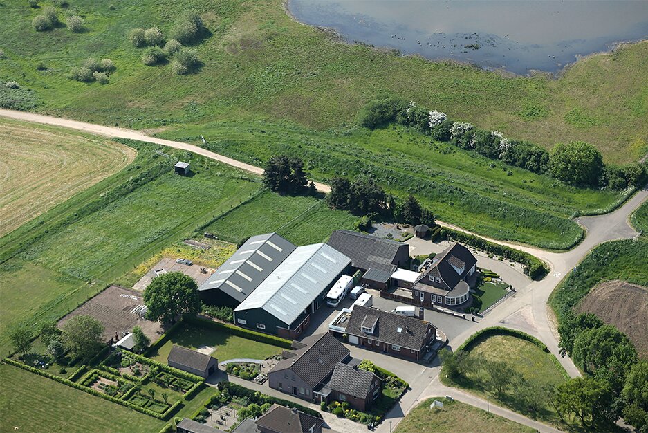 Luchtfoto van de vestiging van Technisch Isolatiebedrijf Nijmegen tussen de weilanden, met het water op de achtergrond