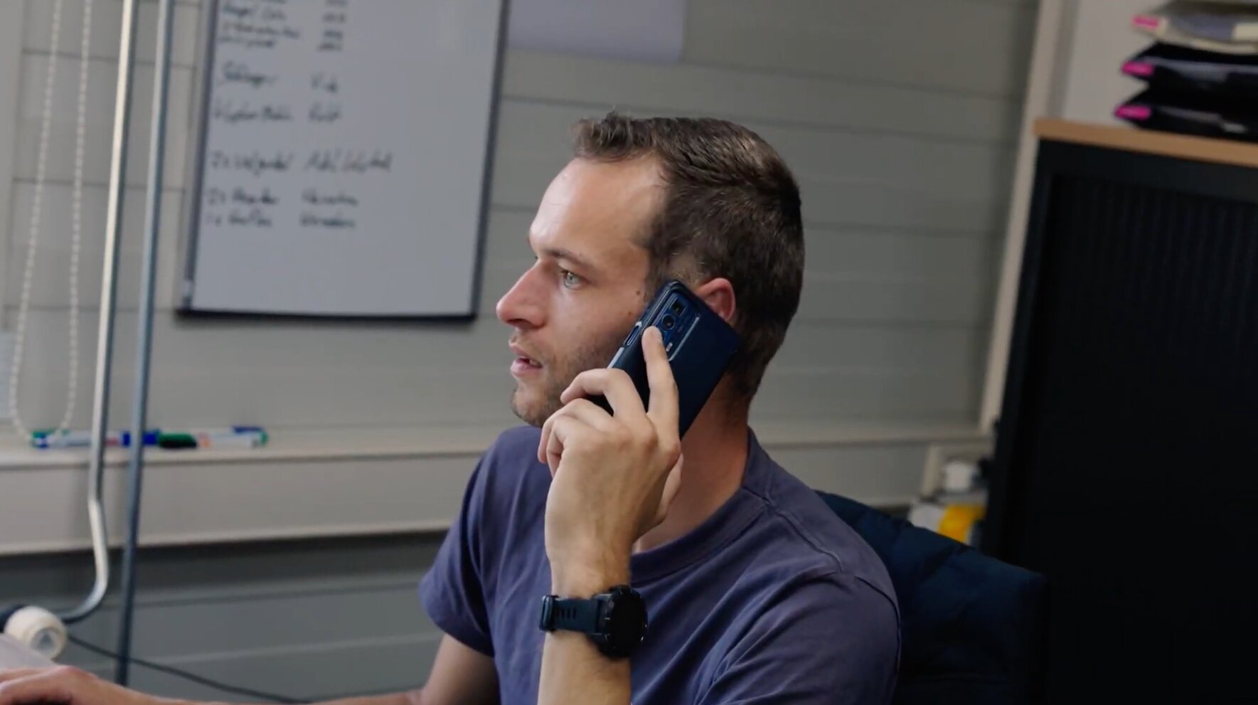 Medewerker aan de telefoon op kantoor met een whiteboard op de achtergrond